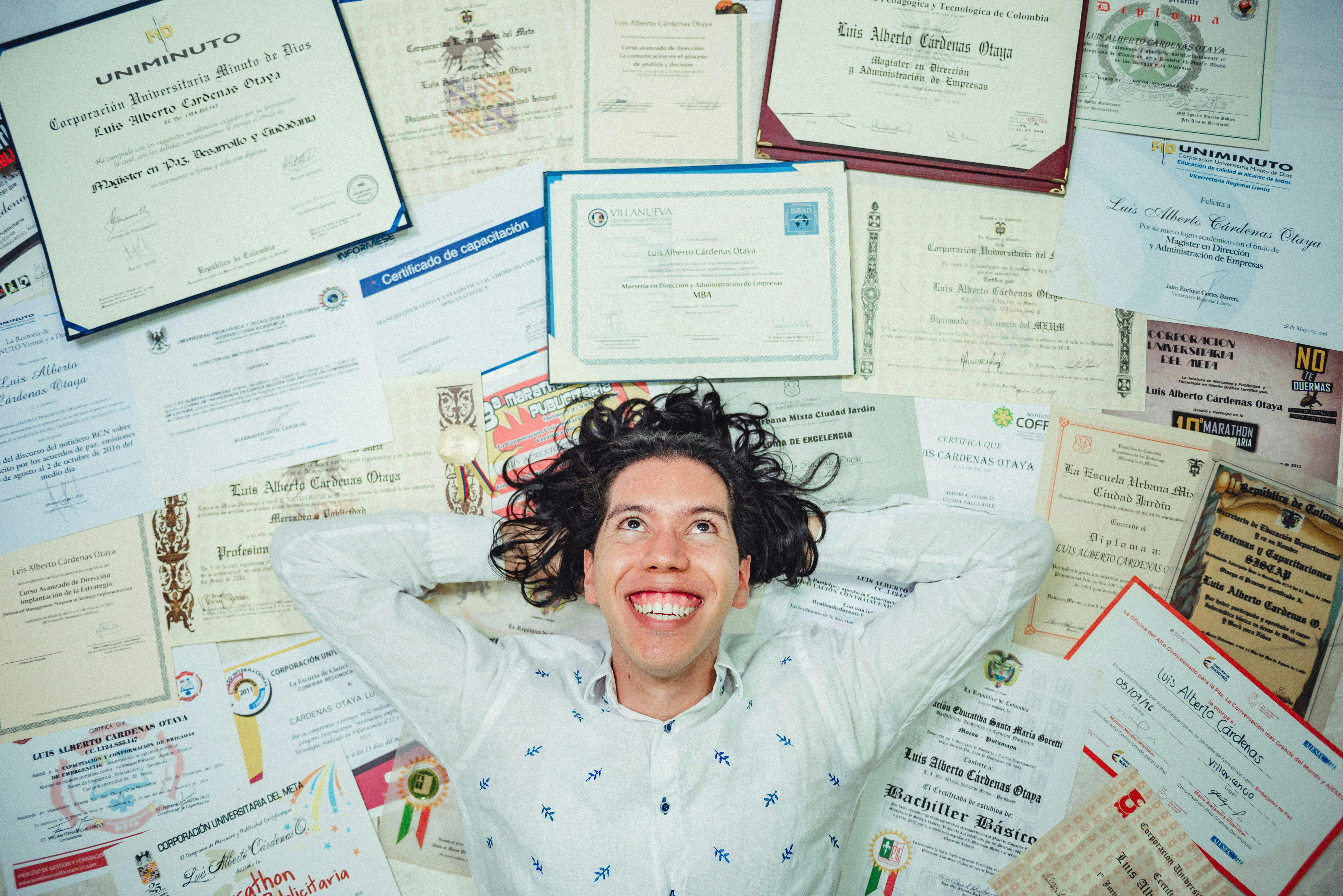 Cesta k úspěchu: Jak vám jazykový certifikát otevře dveře do světa Šťastný mladý muž ležící na zemi obklopený svými diplomy a certifikáty. Obrázek symbolizuje úspěch, akademické úspěchy a výhody získání oficiálního osvědčení.